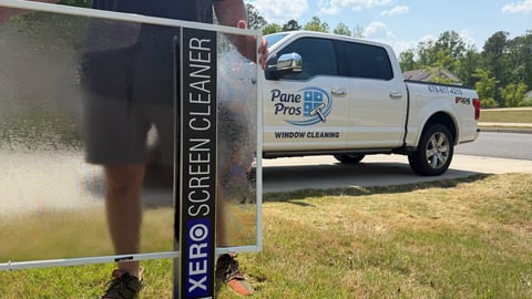 A white Pane Pros window cleaning service truck parked next to a large Xero Screen Cleaner advertisement sign